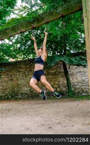 Female athlete doing monkey exercises on rings in a park. Woman doing monkey exercises on rings