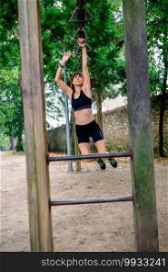 Female athlete doing monkey exercises on rings in a park. Woman doing monkey exercises on rings