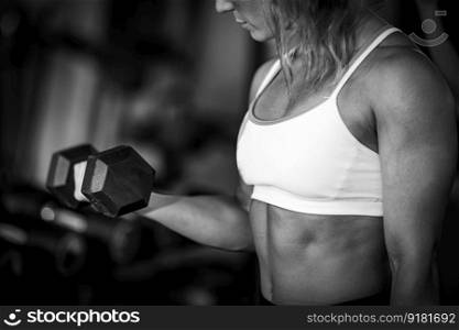 Female athlete exercising with dumbbells in the gym, black and white. Female Athlete Exercising with Dumbbells in the Gym.