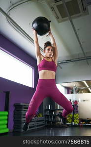 Female athlete practicing wall ball shots with a med ball at the gym.. Female athlete practicing wall ball shots with a med ball