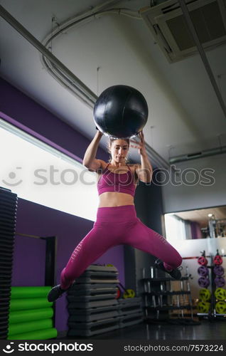 Female athlete practicing wall ball shots with a med ball at the gym.. Female athlete practicing wall ball shots with a med ball