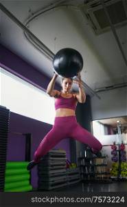 Female athlete practicing wall ball shots with a med ball at the gym.. Female athlete practicing wall ball shots with a med ball