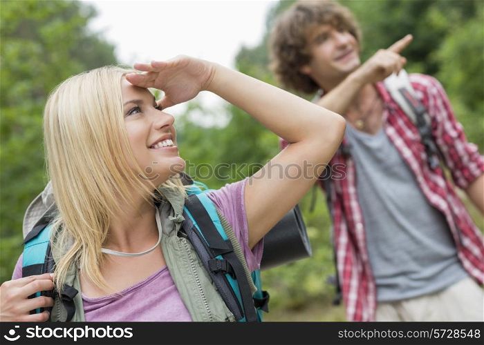 Female backpacker looking away while man showing something in forest