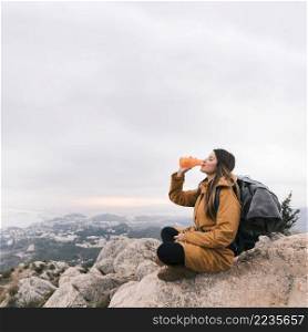 female backpacker sitting top mountain drinking water