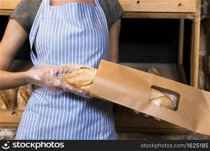 female baker apron packing baguette bread brown paper bag
