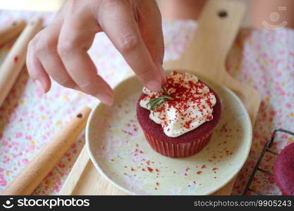 Female baker decorating top cupcake at table before serving.