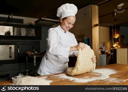 Female baker kneading or forming dough while working at bakehouse. Fresh pizza, pie, bread or sweet pastry preparation process. Female baker kneading or forming dough while working at bakehouse