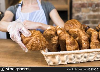 female baker s hand wearing plastic glove taking baked croissant from basket