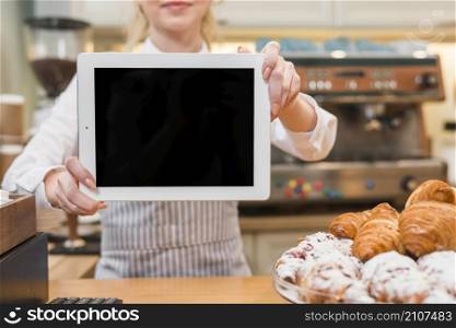 female baker showing digital tablet front baked croissant counter