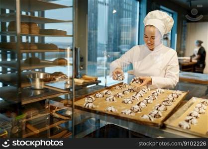 Female baker wearing white uniform laying out freshly cooked cookies. Baking tray with sweet pastry. Female baker in uniform laying out freshly cooked cookies