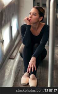 Female ballet dancer sitting on the floor after rehearsal against window full of sunlight