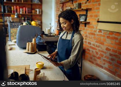 Female barista in apron take orders in cafe. Woman makes fresh espresso in cafeteria, waiter prepares coffee at the counter in bar. Female barista in apron take orders in cafe