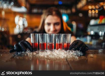 Female barman in gloves puts drinks on ice. Woman bartender mixing at the bar counter in pub. Barkeeper occupation. Female barman in gloves puts drinks on ice