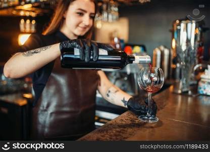 Female barman pours red wine into a glass. Woman bartender working at the bar counter in pub. Barkeeper occupation. Female barman pours red wine into a glass