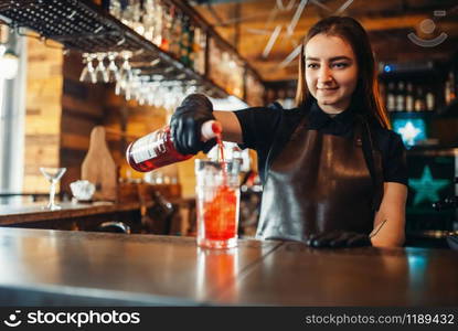 Female barman prepares alcoholic coctail with ice. Alcohol drink preparation. Woman bartender working at the bar counter in pub. Female barman prepares alcoholic coctail with ice