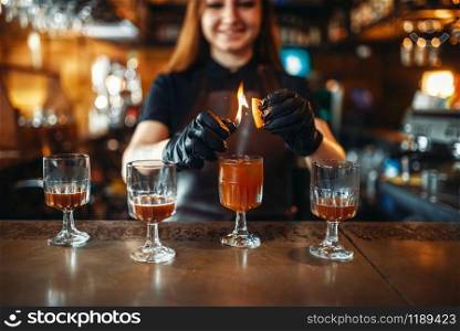 Female bartender making coctail with the use of fire. Alcohol drink preparation. Barman working at the bar counter in pub. Female bartender making coctail with use of fire