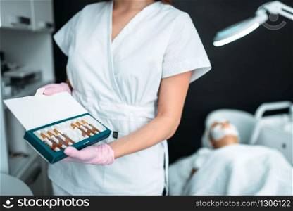 Female beautician shows ampoules with a drug for rejuvenation, cosmetology cabinet. Doctor in white uniform in spa salon, beauty medicine. Beautician shows ampoules, drug for rejuvenation