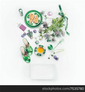 Female beauty flat lay with green high heels , flowers, cup of tea, cakes , cosmetics and blank white paper box. Top view. Layout for your product, design or blog with copy space