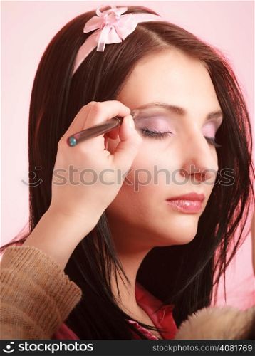 Female beauty. Makeup artist stylist applying with brush violet purple eyeshadow on eyelid of young woman on pink. Girl by visagiste.