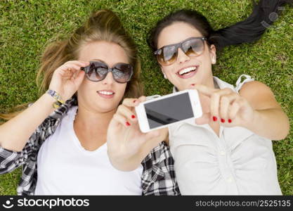 Female best friends lying on the grass and making selfies