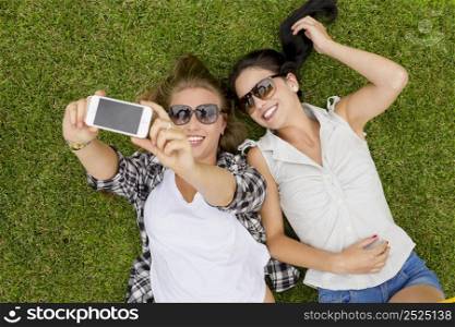 Female best friends lying on the grass and making selfies