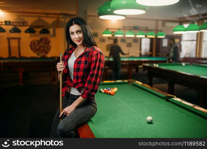 Female billiard player with cue poses at the table with colorful balls. Woman plays american pool game in sport bar