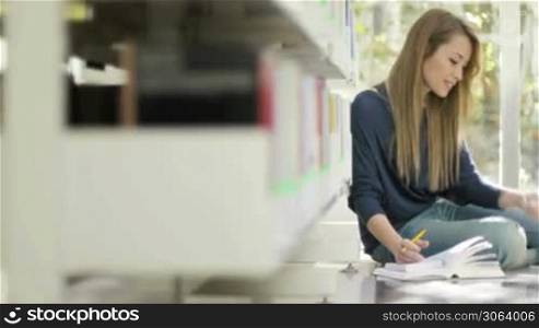 Female blonde college student sitting on floor in library, typing on mobile phone. Dolly shot