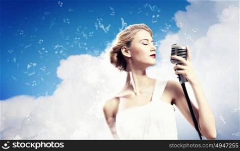 Female blonde singer. Image of female blonde singer holding microphone against clouds background with closed eyes
