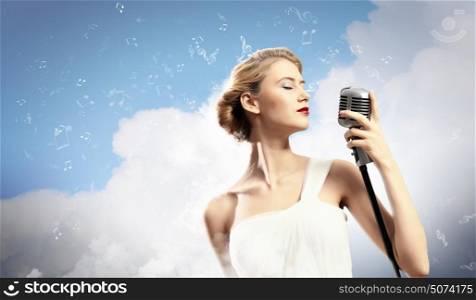 Female blonde singer. Image of female blonde singer holding microphone against clouds background with closed eyes