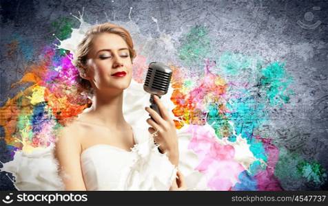 Female blonde singer. Image of female blonde singer holding microphone against color background with closed eyes