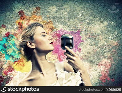 Female blonde singer. Image of female blonde singer holding microphone against color background with closed eyes