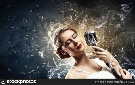 Female blonde singer. Image of female blonde singer holding microphone against smoke background with closed eyes