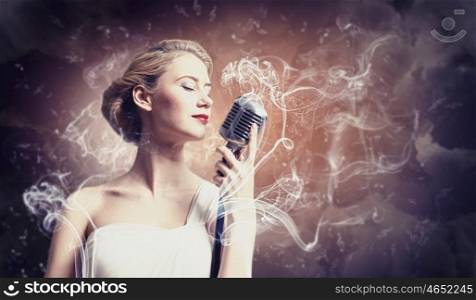 Female blonde singer. Image of female blonde singer holding microphone against smoke background with closed eyes