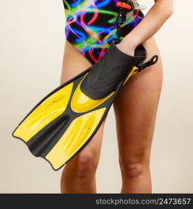 Female body wearing swimsuit holding flippers, studio shot on grey. Girl preparing to summer vacation. Snorkeling swimming concept. Woman in swimsuit holds flippers