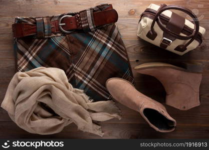 Female boot with bag and checked skirt at wooden table. Modern concept of clothing