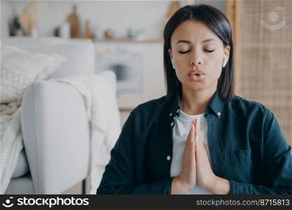 Female breathing deep, listening to meditation in earphones with namaste gesture at home. Calm woman meditates after hard day, listens to relaxing music. Stress relief, healthy lifestyle concept.. Female breathing deep, listens to meditation in earphone with namaste gesture at home. Stress relief