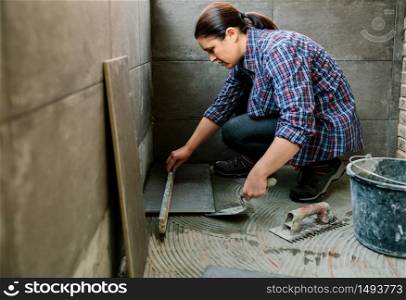 Female bricklayer checking the floor with a level to install a tile floor. Female bricklayer checking floor with a level