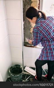 Female bricklayer leveling cement with a trowel to tile the wall. Bricklayer leveling cement with a trowel to tile the wall