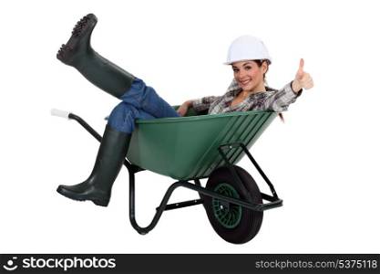 female bricklayer sitting in wheelbarrow thumb up