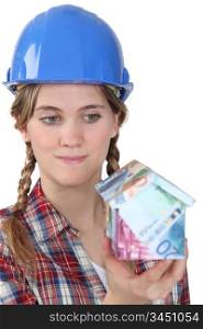 Female builder holding house made from bank notes