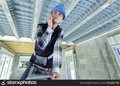 female builder on stepladder inspecting the roof