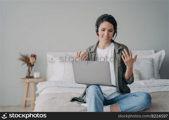Female business coach in headset talk, consult client on video call on laptop at home. Smiling woman self employed freelancer teacher conducts online lesson of language. Elearning, distant work.. Female freelancer teacher in headset conducts online lesson at laptop. Elearning, distant work