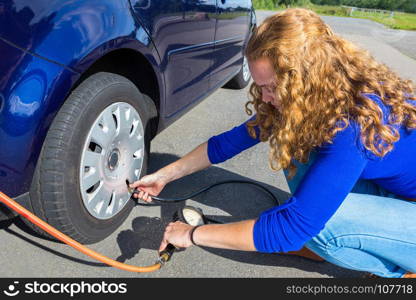 Female car driver checking air pressure of tire outside