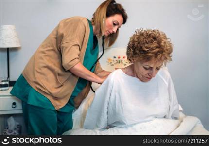 Female caregiver auscultating senior woman at home. Caregiver auscultating senior woman