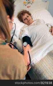 Female caregiver checking blood pressure to a senior woman at home. Caregiver checking blood pressure to a senior woman