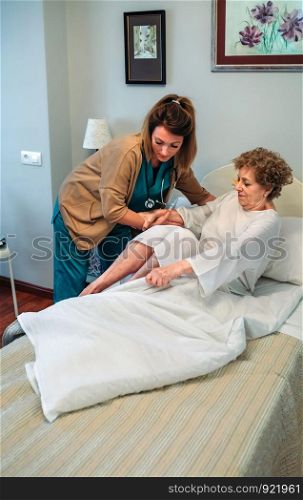 Female caregiver helping elderly female patient to get out of bed. Caregiver helping elderly patient to get out of bed