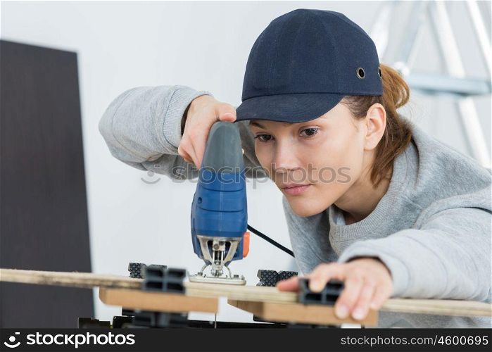 female carpenter cutting wood with jigsaw in workshop