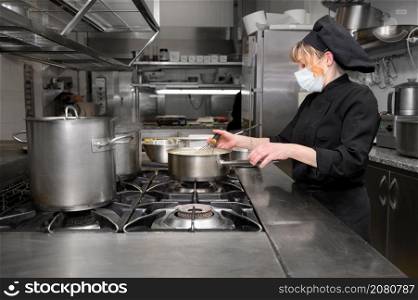 Female chef cooking in the kitchen at restaurant wearing protective medical mask in coronavirus new normal concept. High quality photo. Female chef cooking in the kitchen at restaurant wearing protective medical mask in coronavirus new normal concept.