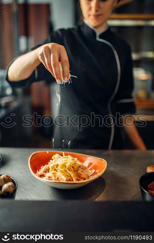 Female chef cooking pasta with cheese in a bowl on wooden table. Garnish for stek, food preparation on kitchen