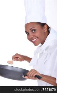 Female chef in uniform with a deep frying pan and wooden spoon